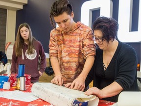 Denise Deiana, right, and Benjamin Morrow, centre, wrap a christmas gift containing Saskatchewan Roughriders merchandise during a sustainable gift-wrapping service being offered at the Northgate Mall. Jenna Rae Donison looks on from behind. A group of Winston Knoll students and parents are using donated antique blueprints to wrap the gifts as a way of reusing the paper.