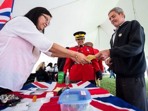 Dwayne Kline, right, a member of Cowessess First Nation who resides in Regina, hands a slip indicating his eligibility for a treaty annuity payment of five dollars to Geraldine Linton, left, a governance officer for Indigenous Services Canada, in Regina on June 5, 2018. Behind them, Inspector Honey Dwyer of the RCMP looks on.
