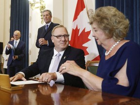 Scott Fielding, MLA for Kirkfield Park, centre signs documents with Lieutenant Governor Janice Filmon after he is sworn into cabinet as the new minister of Finance and minister responsible for the civil service during Premier Brian Pallister's cabinet shuffle announced at the Manitoba Legislature in Winnipeg on August 1, 2018. The Manitoba government is making its tax credit for film and video productions permanent. Sport, Culture and Heritage Minister Cathy Cox says the credit, which was set to expire at the end of this year, has attracted projects and boosted the economy. Finance Minister Scott Fielding says the province will offer more to the film and video industry in the spring budget, which is expected in March, but he would not reveal details.