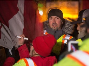 Supporters of a truck convoy headed to Ottawa sign a flag mounted on one of the trucks sitting on the service road off Highway 1 near the Prairie Oasis motel in Moose Jaw as the convoy makes a stop. Rion White of Moose Jaw can be seen wearing a toque at centre.