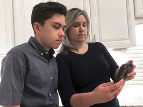 FILE- In this Jan. 31, 2019, file photo Grant Thompson and his mother, Michele, look at an iPhone in the family's kitchen in Tucson, Ariz., on Thursday, Jan. 31, 2019. Apple has released an iPhone update to fix a FaceTime flaw that allowed people to eavesdrop on others while using its group video chat feature. The repair is included in the latest version of Apple's iOS 12 system, which became available to install Thursday. Apple credited the Tucson teenager, Grant Thompson, for discovering the FaceTime bug.