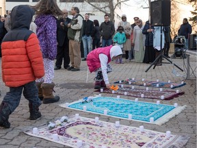 A girl lays flowers on a prayer rug lined with candles at a vigil held at Regina City Hall for the victims of the terror attacks in Christchurch, New Zealand.