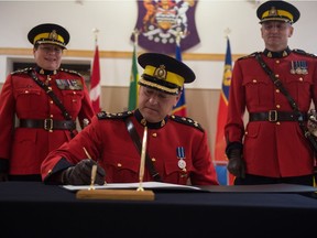 RCMP 'F' Division Commanding Officer Mark Fisher, centre, signs a document as he takes command from former C/O Curtis Zablocki, right, at RCMP depot on Dewdney Avenue.