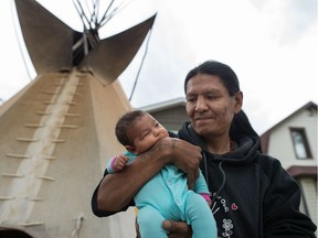 Prescott Demas stands holding his 10-week-old daughter Tema Demas in a front yard on Cameron Street where he has erected the teepee that once served as the centrepiece for the Justice for our Stolen Children camp.