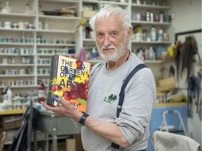 Victor Cicansky stands in his studio, holding a ceramic book he made entitled The Garden of Art.