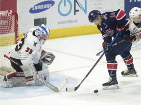 Moose Jaw Warriors goalie Bailey Brkin keeps an eye on the puck as Regina Pats captain Austin Pratt fights off a check during WHL action at the Brandt Centre on Friday.