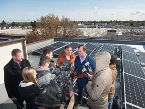 NDP MLA Trent Wotherspoon addresses the media regarding his party's position on the province's recently scrapped net metering program. Standing next to Wotherspoon, in an orange jacket, is NDP MLA Yens Pederson. The news conference was held on the roof of a building on Rae Street, upon which a solar array has been installed to provide the building with electricity.