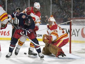 Calgary Flames defenceman Travis Hamonic, 24, checks the Winnipeg Jets' Mathieu Perreault, 85, in front of goalie David Rittich during the NHL Heritage Classic at Mosaic Stadium on Saturday.