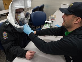Staff Sgt. Brad Walter, left, and Cst. Tyler Lerat demonstrate part of the fitment process for respiratory protection masks being undertaken by the Regina Police Service at the service's headquarters on Osler Street in Regina, Saskatchewan on Mar. 19, 2020. The masks will be used to protect front line officers against the COVID-19 virus in instances where they need to come into contact with an individual who may have the virus. The hood worn by Walter is used during fitment only. A scent is introduced into the hood to ensure proper mask fitment.