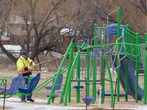 A worker wraps "caution" tape around a playground structure in the Kiwanis Park area during the COVID-19 pandemic in Regina on March 25.