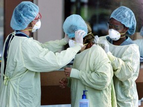 Health care workers help a visitor going to the intensive care unit put on a gown and mask to protect against contracting Severe Acute Respiratory Syndrome (SARS) at North York Hospital in Toronto, May 29, 2003.