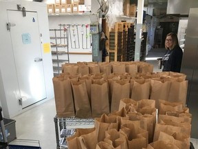 Bagged lunches sit ready for delivery inside the Indian Head Bakery as Lisa Horsman, who owns the bakery with her husband Bart, looks on. All the meals were paid for by donations as part of the High Five campaign the bakery is running to support those impacted by COVID-19.