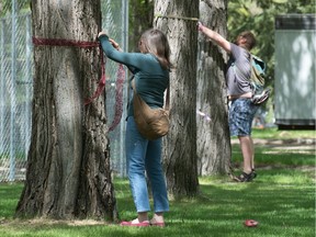 People wrap ribbons around trees in Wascana Park near the new Conexus Credit Union Building in Regina, Saskatchewan on May 27, 2020. Roughly 69 trees are allegedly at risk of demolition to make way for the City of Regina's proposed aquatic destination facility.