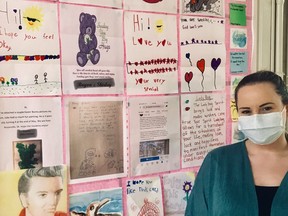 Jillyan Clark, recreation coordinator at the Qu'Appelle House Seniors Care Home in Regina, stands in front of a wall covered in art children in the community have mailed in to cheer up the care home's residents. (Photo courtesy of Jillyan Clark)