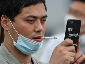 A man smoking a cigarette over a face mask takes a photo at the promenade on the Bund along the Huangpu River during a holiday on May Day, or International Workers' Day, in Shanghai on May 1, 2020.