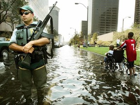 A police officer keeps watch as people walk through water in downtown after Hurricane Katrina on Aug. 31, 2005 in New Orleans. A total of 1,833 deaths were attributed to the hurricane. COVID-19 has killed more people in a single day.