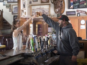 Greg Hooker, co-owner of Victoria's Tavern, hands a pint over the newly installed plexiglass to Chantelle Kraushaar, general manger, on June 5, 2020.  Once partially opened on June 8, this won't be the way they distribute drinks, but did it for illustration purposes to show new safety measures of the plexiglass.  TROY FLEECE / Regina Leader-Post