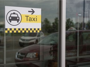 A taxi sign can be seen on the window of the Regina International Airport in Regina, Saskatchewan on June 30, 2020. In the reflection of the window, a Captial Cabs taxi can be seen.