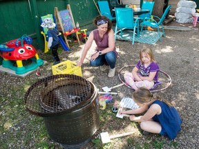 Lisa Stretten, left, owner of licensed home day care Kinder Explorers, watches as Lilith Edge, centre, and Rowan Roberts paint garden signs at her home in Regina, Saskatchewan on June 10, 2020.