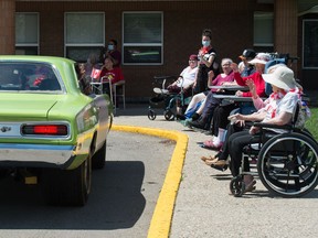 Passengers in a classic car wave as a parade of cars drives past a line of residents and workers at the William Booth Special Care Home in Regina, Saskatchewan on July 1, 2020.