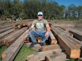 Tyler Slowski, owner of Prairie Barn Brothers, sits on a stack of reclaimed lumber from an old barn dismantled by the company on a worksite just outside of Regina, Saskatchewan on July 29, 2020.