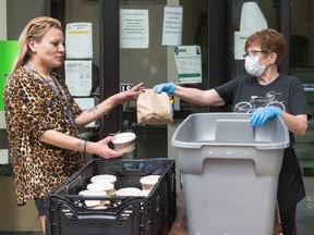 Volunteer coordinator Rhonda Mills, right, hands a lunch to guest Glenda Whitebird in front of Carmichael Outreach during the organization's lunch service at its 12th Avenue office in Regina, Saskatchewan on July 15, 2020.