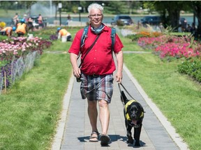 Kerry Macdonald, a volunteer puppy raiser with the Canadian National Institute for the Blind, walks with guide dog Indy in the park across from the Saskatchewan Legislative Building in Regina on July 22, 2020. Indy was part of a class of guide dogs that recently completed part of their training in Saskatchewan as part of a relatively new training program.