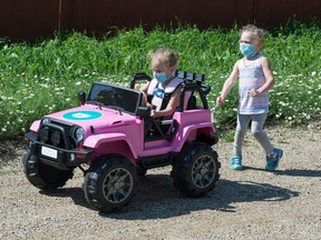 Mila Winkler watches as her twin sister Bella Winkler drives a toy jeep the pair had donated to them through funding raised by the SaskMasks program at a media event held near the Winkler family home in Regina, Saskatchewan on July 24, 2020. The twins have cerebral palsy, and the jeep has been modified to make it usable for them to play in. SaskMasks was started in March by a team of University of Regina students who made and sold masks and raised more than $30,000 for various charities in Regina.