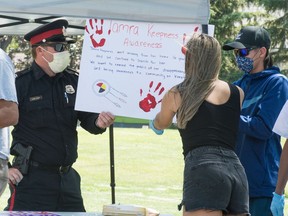 A police officer helps others present hang a sign during an event held in the absence of a long-running annual barbecue to raise awareness about missing person Tamra Keepness (cancelled due to COVID-19) in Regina, Saskatchewan on July 17, 2020.