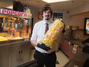 Thomas Hendricksen, manager at the Rainbow Theatre, stands holding an oversized bag of popcorn in the theatre's concession area in the Golden Mile Mall in Regina, Saskatchewan on July 18, 2020. The theatre plans to reopen soon and is selling bags of popcorn in the interim.