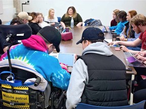 Mia Bell, University of Regina masters student and Mitacs intern at VOICE Lab (far centre), sits at a table at the U of R with Astonished! Inc members. The members are using an app called Thisissand to create virtual art.