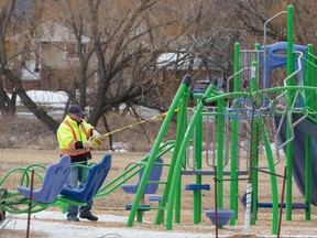 A worker wraps "caution" tape around a playground structure in the Kiwanis Park area during the COVID-19 pandemic in Regina on March 25, 2020.