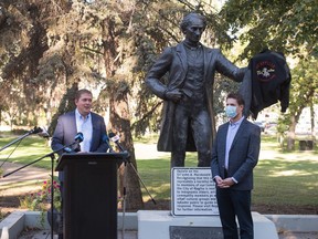 Conservative Party of Canada (CPC) MP Andrew Scheer, left, speaks at a "virtual rally" broadcast over the internet, regarding the pictured statue of John A. Macdonald in Victoria Park in Regina on Sept. 3, 2020. Standing in front of the statue is CPC MP Michael Kram. A jacket with the words Qu'Appelle Indian Residential School embroidered on it is seen hanging on the arm of the statue.