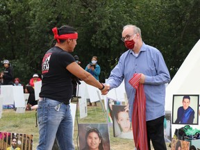 Chris Merasty, who walked with Tristen Durocher from Northern Saskatchewan, hands Court of Queen's Bench Justice Graeme Mitchell a Metis sash outside Durocher's teepee last September.