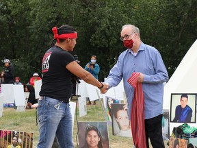 Chris Merasty, who walked with Tristen Durocher from northern Saskatchewan, hands Court of Queen's Bench Justice Graeme Mitchell a Metis sash outside Durocher's teepee in Wascana Centre on Sunday, Sept. 13, 2020 in Regina, Saskatchewan.