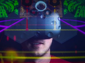 Taylor Eichhorst of BitCutter Studios stands in his home office wearing an HTC Vive virtual reality headset.  The game designer works on games that utilize virtual reality. The game Groove Gunner is superimposed over Eichhorst by way of an in-camera double exposure, giving the viewer a look at what he sees when playing the game.