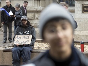 A man holds a sign up behind organizers of an event in April 2019 protesting against Saskatchewan having the lowest minimum wage in the country.