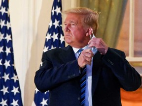 President Donald Trump pulls off his protective face mask Monday as he poses atop the Truman Balcony of the White House after returning from being hospitalized.