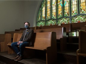 Minister Cameron Fraser sits in the pews at the Knox Metropolitan United Church with the iconic stained glass windows in the background.