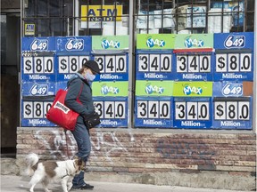 In this file photo, a pedestrian wearing a mask and walking her dog walks past Lotto Max and Lotto 649 advertising on Toronto's Broadview Avenue in October 2020.