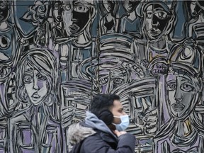 A masked pedestrian walks in downtown Regina by a mural.