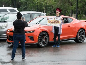 Emilio Bosch, a grad from Leboldus High School, stands for his photo in front of a car owned by another grad during a "grad parade" event held near the Saskatchewan Legislative Building in Regina, Saskatchewan on June 28, 2020.
