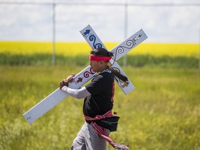 A man carrying a cross marches with Walking With Our Angels, a group that walked from La Ronge to Regina in the summer of 2020 to demand provincial action on suicide prevention. Photo taken in Saskatoon on July 17, 2020.