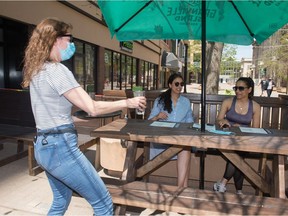 Julie Nickerson, general manager of the Fat Badger, brings waters out to Jyoti Juttla, centre, and Vibha Zafar on the patio from the restaurant on Scarth Street in Regina, Saskatchewan on May 17, 2021.