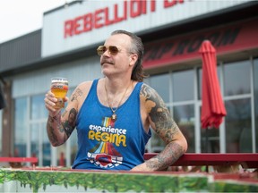 Rebellion Brewing owner Mark Heise sits outside the brewery's taproom in Regina, Sask. on May 26, 2021, showing off an Experience Regina glass and shirt, which are part of a new Hop Circuit organized by the brewery.