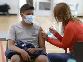 Public health nurse Karen Baily delivers a dose of Pfizer COVID-19 vaccine into the arm of Scott Collegiate student Rashawn Taniskishayinew at the mâmawêyatitân centre in Regina, Saskatchewan on May 31, 2021.