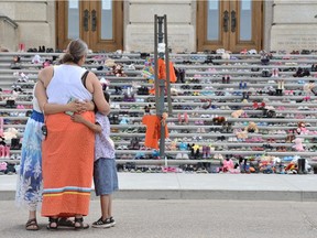 People embrace while observing a display of children's shoes representing children who died while in Canada's residential school program on the steps of the Saskatchewan Legislative Building in Regina, Sask. on May 31, 2021.