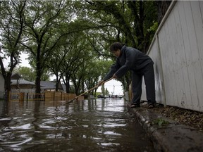 Joanna Koskamp, a resident of the 1700 block Quebec Street, uses a rake to try and clear debris from the storm drain in Regina on June 11.