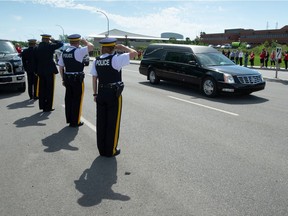 RCMP members salute while watching a procession of police vehicles following a hearse down Dewdney Avenue in Regina, Saskatchewan on June 15, 2021. The procession passed by RCMP 'F' Division headquarters Tuesday following the June 12 on-duty death of RCMP Const. Shelby Patton in Wolseley, Saskatchewan.