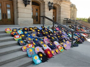 Children's backpacks, many of which have orange handprints affixed to them, are seen laying in front of the Saskatchewan Legislative Building in Regina on June 29, 2021. Prairie Crowe initially organized the display to honour those in unmarked graves by the former residential school on Cowessess First Nation and urged others on social media to bring more in hopes of having 751 on the steps for Canada Day.